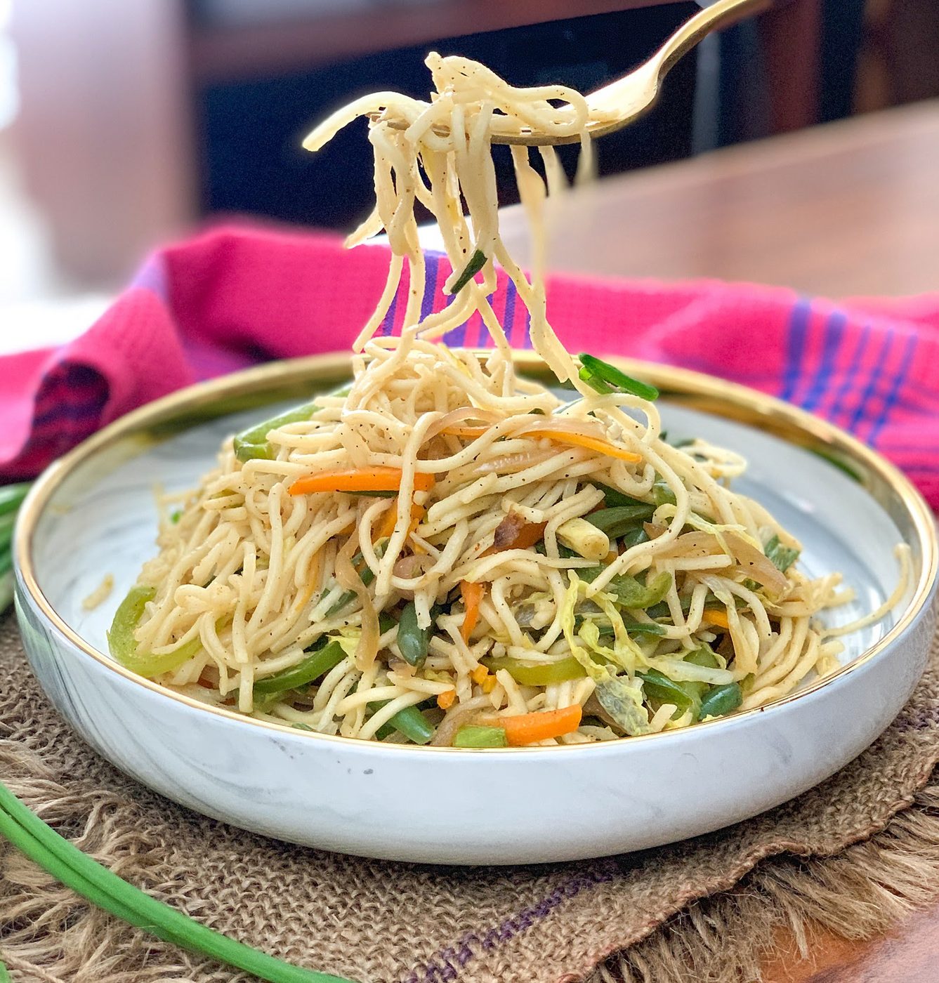 Spring onion oil noodles with sliced vegetables on a white plate, with noodles lifted on a fork