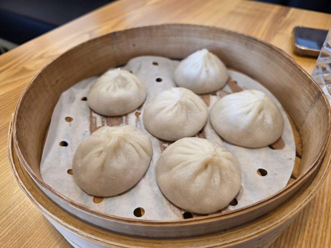 Six pale handmade steamed bao arranged in a bamboo steamer on a wooden table